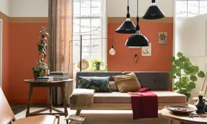 Wohnzimmer mit orangefarbenen Wänden, die mit abriebfester Farbe gestrichen sind. Ein Sofa, ein Tisch mit Büchern und Pflanzen.
