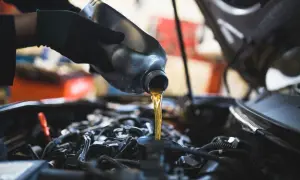 Main d'un mécanicien versant de l'huile neuve dans le moteur d'une Dacia Sandero lors d'une vidange.