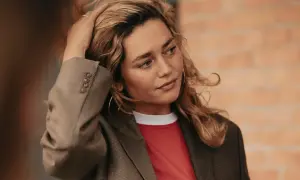 Kobieta z blond włosami w marynarce i czerwonej koszulce, dotykająca włosów.