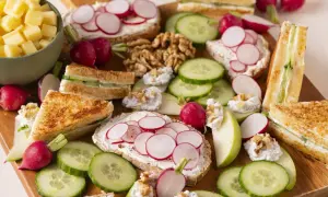 Un plateau d'apéro dinatoire plancha : toasts au fromage frais et radis, mini sandwichs concombre, dés de fromage, noix et quartiers de pomme.