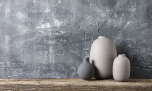 Nowoczesny tynk strukturalny do łazienki w odcieniu szarości, z trzema ceramicznymi wazonami na drewnianej półce.