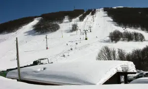 Piste innevate e skilift attivi sul monte Piselli, stazione sciistica con alberi spogli e cielo azzurro.
