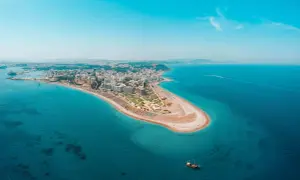 Luftfoto över Rhodos kustlinje med en sandstrand, hotell och turkost vatten. En segelbåt syns i vattnet, perfekt för Rhodos aktiviteter.