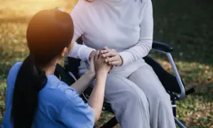 Un infermiere tiene le mani di una paziente su una sedia a rotelle, un gesto di conforto e cura. L'età non conta, l'assistenza è l'essenza.
