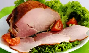 Pieczona szynka peklowana z sałatą i pomidorkami na białym talerzu.