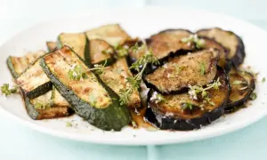 Gebratene zucchini und aubergine in der pfanne, garniert mit frischen Kräutern.
