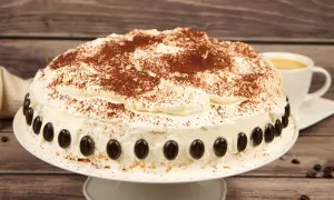 Eine köstliche Cappuccino Torte, einfach zubereitet, mit Kakao bestäubt und mit Kaffeebohnen dekoriert. Daneben eine Tasse Kaffee.