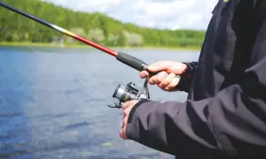 Mann hält Angelrute und Rolle am See. Perfekter Ort, wo kann ich angeln?