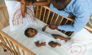 Parents hold their baby's hand in a crib with a breathable mattress, a safe sleep environment.
