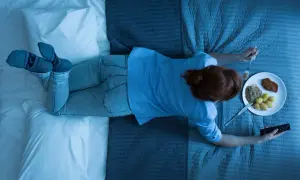 A woman eats dinner in bed, holding a remote. Wondering how long should you wait to sleep after eating?