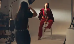 Modelka w czerwonym garniturze pozuje do zdjęć. Fotografka wykonuje zlecenia, łapiąc kadr.