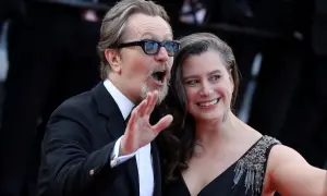 Gary Oldman z żoną, uśmiechnięci i pełni życia, pozują do zdjęć na czerwonym dywanie.