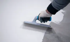 Mano con guanto stende resina, mostrando la differenza tra resina epossidica e poliuretanica per pavimenti.