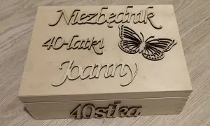 Drewniana skrzynka z napisem "Niezbędnik 40-latki Joanny" i motylem. Na froncie "40stka".