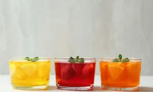 Trzy galaretki w szklankach: cytrynowa, truskawkowa i pomarańczowa, ozdobione miętą.