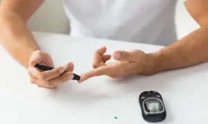 Mężczyzna wykonuje badanie poziomu cukru we krwi za pomocą glukometru. Na stole leży glukometr i pasek testowy.