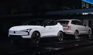 Dwa białe, nowe Volvo na czarnej scenie. Jedno z przodu z charakterystycznymi światłami, drugie z tyłu z nowoczesnymi lampami.