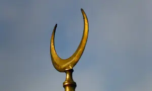 Złoty półksiężyc, symbol meczetu, na tle błękitnego nieba.