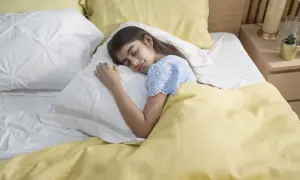 A young girl sleeps peacefully under a yellow blanket. This serene scene reminds us of the importance of fresh air and how to get rid of off-gassing smells for a healthy sleep environment.