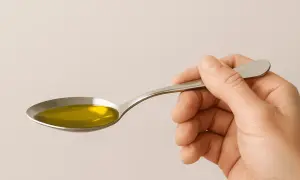 Una cuchara sostiene aceite de oliva dorado, un alimento que contiene vitamina D.