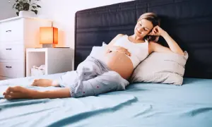 Kobieta w ciąży leży na łóżku, dotykając brzucha. Zastanawia się nad pierwszymi objawami ciąży, w tym zmianami śluzu.