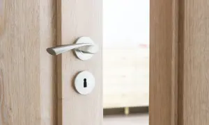 Drewniane drzwi z metalową klamką i otworem na klucz, uchylone.