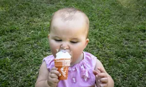 Kleines Baby mit Eiscreme im Gras. Ab wann Eis baby? Diese süße Erfahrung beginnt oft, wenn die Kleinen neugierig werden.