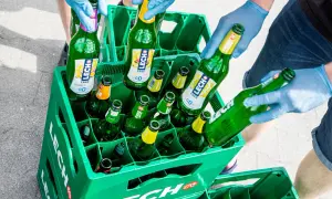 W zielonej kracie Lech Free jest 12 piw. Ręce w niebieskich rękawiczkach układają butelki.