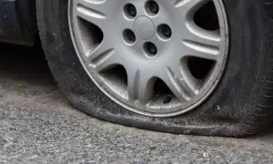 Gros plan sur une roue de voiture avec un pneu dégonflé, posée sur un trottoir gris. La jante est en alliage argenté.