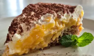 Ein saftiger Apfelkuchen-Schnitte mit cremiger Füllung, Kakao bestäubt und Minze garniert.