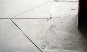 Widoczna dylatacja posadzki przy ścianie, z widocznymi nierównościami i ubytkami w betonie.