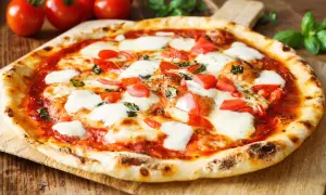 Pyszne ciasto na pizzę bez wyrastania, z pomidorami, mozzarellą i bazylią, na drewnianej desce.
