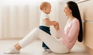 Une mère et son bébé se tiennent la main, souriants, assis sur le sol.