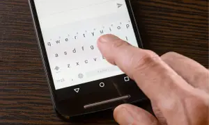 Dłoń pisze SMS-a na telefonie, klawiatura wyświetla litery. Widoczny przycisk "Polski" sugeruje, że problemem jest brak polskich znaków w sms.