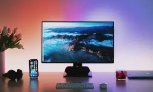 Biurko z monitorem wyświetlającym krajobraz, telefonem, słuchawkami i kubkiem herbaty.