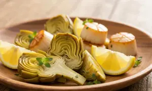 Assiette de Saint-Jacques poêlées et fleur d'artichaut coupée, garnie de quartiers de citron et de quelques herbes fraîches.