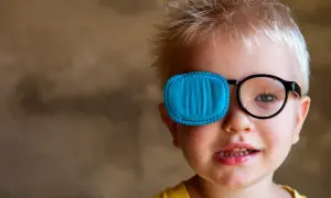 Chłopiec z zasłoniętym jednym okiem niebieską łatką, w okularach. Różne rodzaje zeza wymagają różnych metod leczenia.