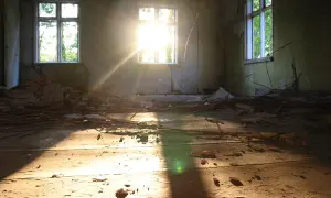 Słońce wpada przez okna zniszczonego pokoju, oświetlając gruzy i deski na podłodze. To miejsce, jakby zapomniane przez czas, czeka na nowy początek, może na rynku wtórnym znajdzie nowe życie.