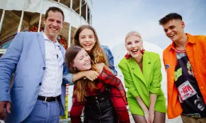 Eine fröhliche Familie genießt den Tag in Berlin. Vater, Mutter und drei Kinder lachen ausgelassen vor einer futuristischen Kulisse.