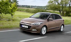 Brązowy Hyundai i20 jedzie po drodze, za nim zielone pola i domy. Sprawdź atrakcyjną hyundai i20 cena!