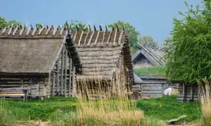 Drewniane chaty kryte strzechą, jak w skansenach w Polsce, stoją nad wodą.