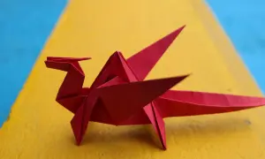 Un dragón rojo de papiroflexia fácil descansa sobre una superficie amarilla y azul.