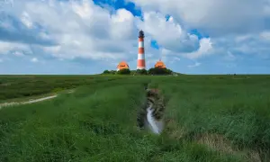 Leuchtturm Westerheversand, ein ikonischer fotospot in Schleswig-Holstein, ragt über grünes Marschland unter dramatischem Himmel.