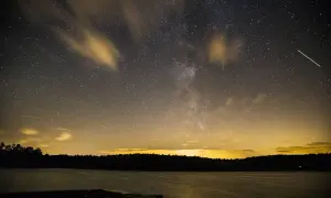 Nocne niebo nad jeziorem, pełne gwiazd i smug chmur, idealne do nauki, jak fotografować gwiazdy. Widać Drogę Mleczną i spadające gwiazdy.
