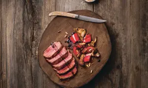 Saftige Tagliata di Manzo mit gebratenen Pilzen und Paprika auf einem rustikalen Holzbrett, garniert mit Pinienkernen und Balsamico.