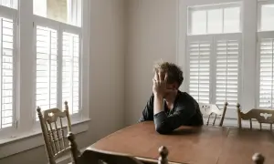 Uomo seduto a un tavolo, con la mano sul viso, immerso in pensieri profondi. Un momento di introspezione, dove mettersi in discussione è parte del percorso psicologico.