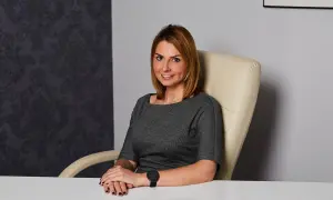 Kobieta w szarej sukience siedzi przy biurku w nowoczesnym biurze.