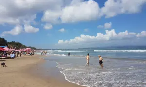 Słoneczny dzień na plaży w Seminyak na Bali. Ludzie spacerują po piasku i kąpią się w oceanie.