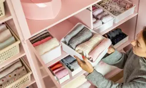 Una mujer organiza su armario, doblando ropa en contenedores. Aprende como ordenar un armario para tener todo a la vista y ordenado.