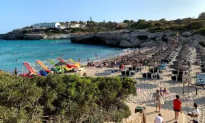 Słoneczna plaża Cala Domingos z kolorowymi zjeżdżalniami wodnymi, rzędami parasoli i turystami cieszącymi się słońcem i morzem.